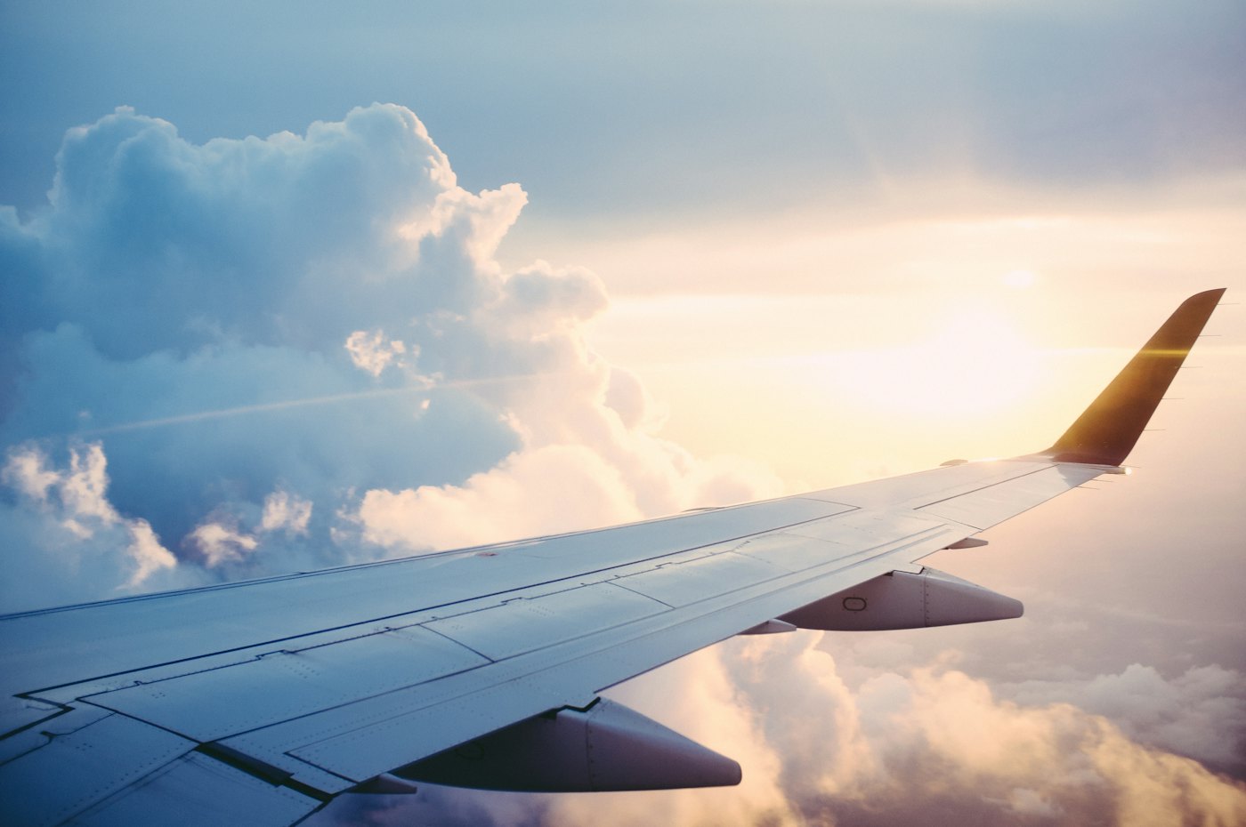 An airplane wing above clouds, with the sun low on the right.