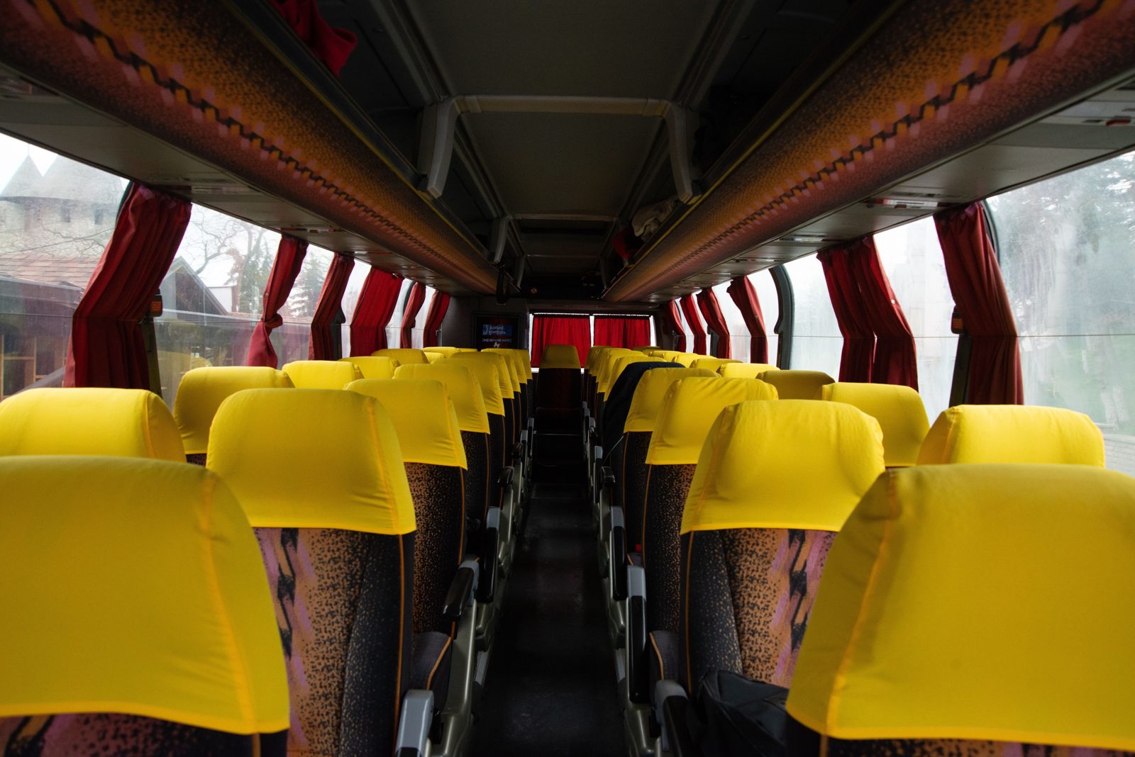 Rows of bright yellow seat covers in an empty coach, red curtains tied at the side windows, and a black bag tucked under a seat on the right of the aisle.